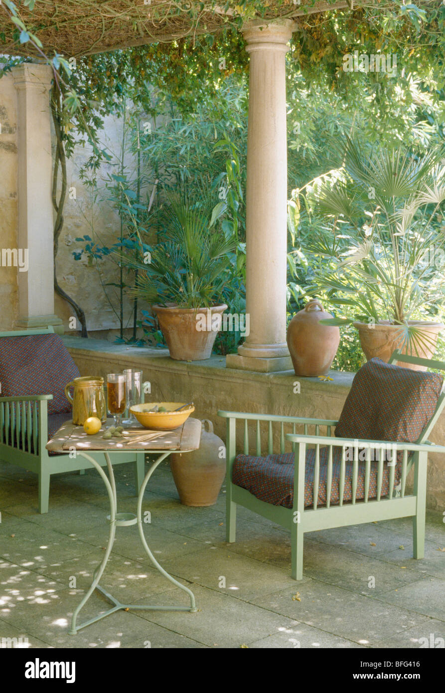 Verde pallido con sedie in legno e metallo piccolo tavolo sulla veranda con pilastri e basso muro di pietra della casa francese di campagna Foto Stock