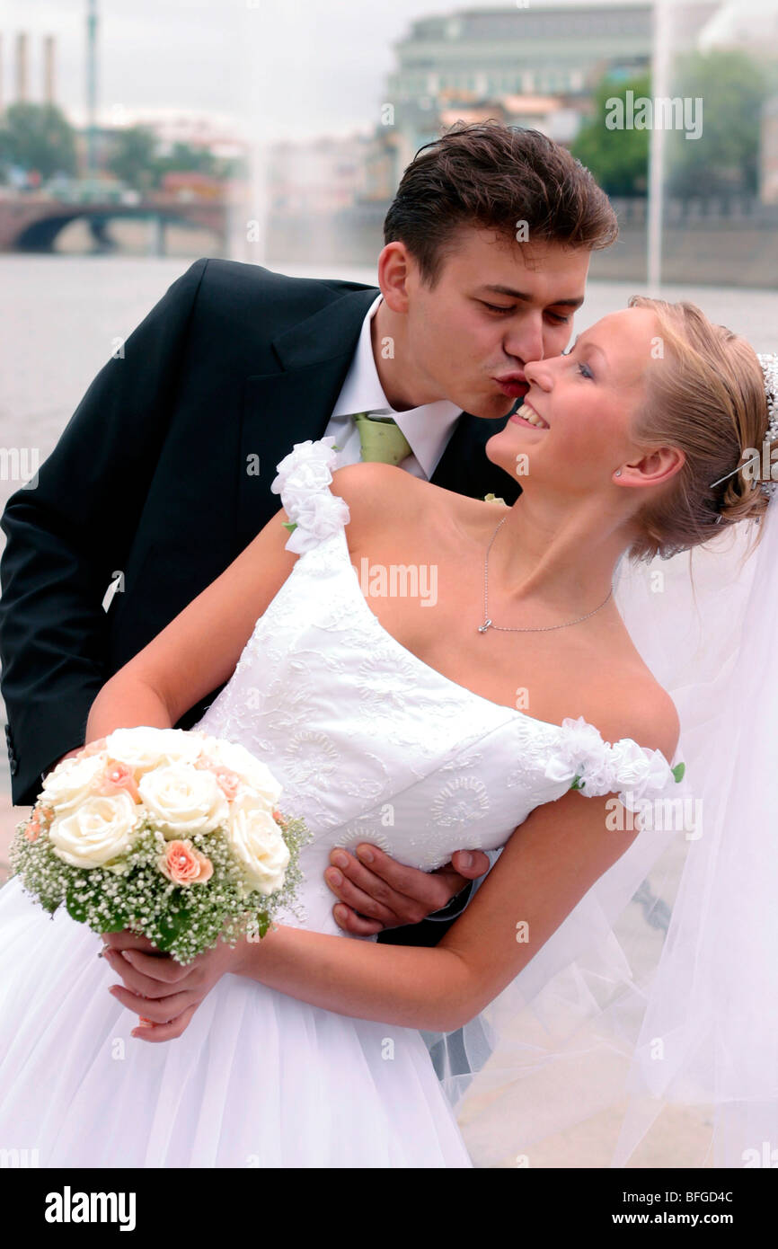 Giovane sposa giovane kissing all'aperto con il fiume in background scena urbana. Foto Stock