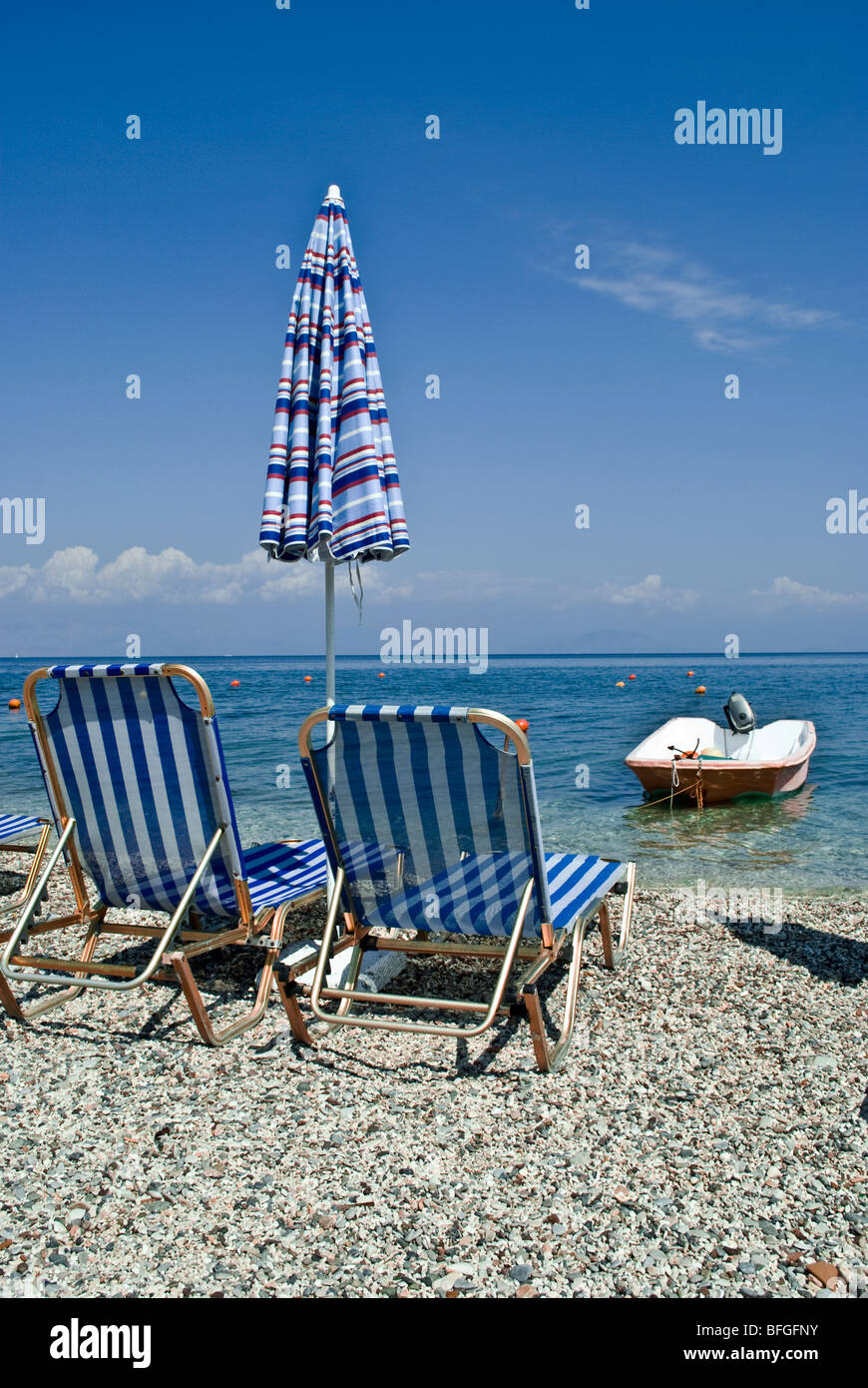 Due sdraio in spiaggia da un ombrello chiuso nella parte anteriore di un bagnino della barca a Benitses (Corfù) Foto Stock