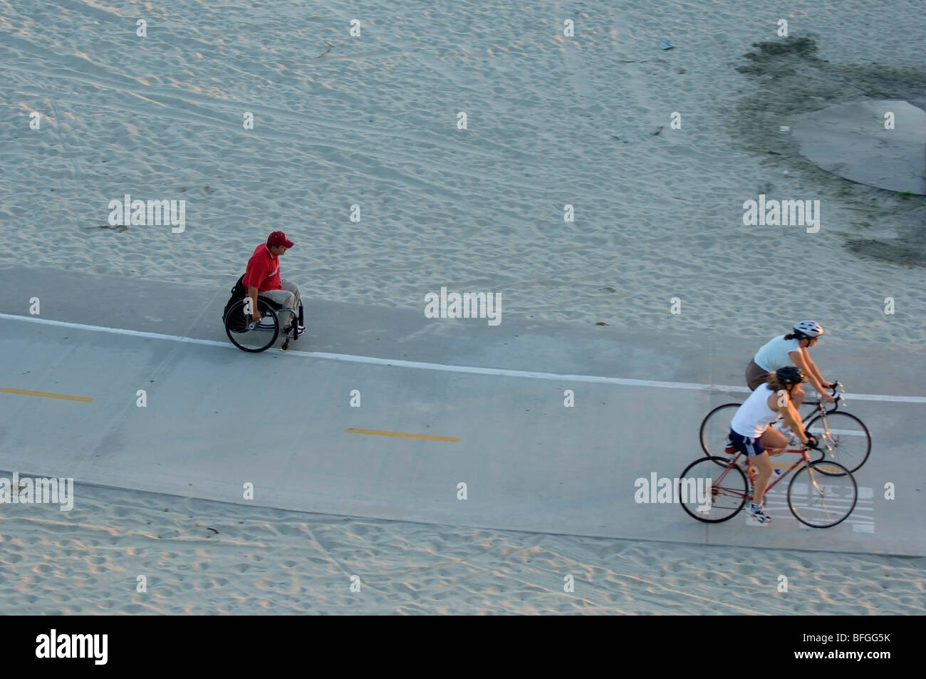 Due piloti di bicicletta il passaggio di una persona disabile che esercitano in una sedia a rotelle sulla stessa pista ciclabile. Foto Stock