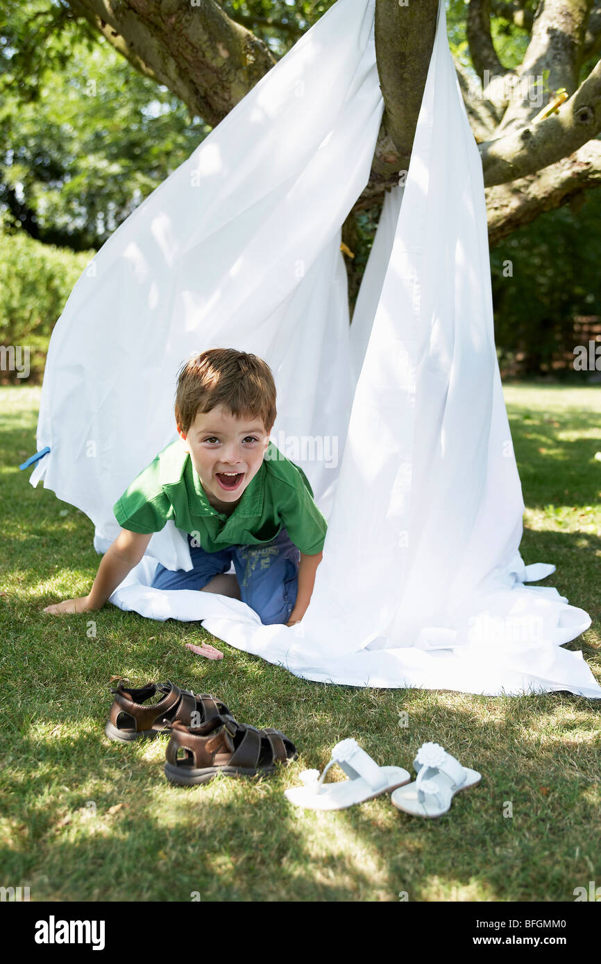 Giovane ragazzo in back yard strisciando fuori della tenda realizzata di lamiera letto, ritratto Foto Stock