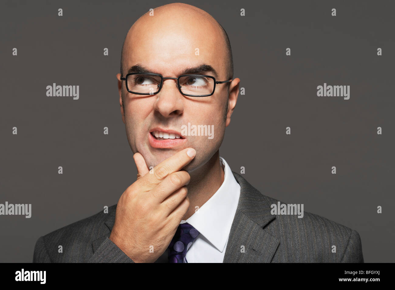 Imprenditore calvo con gli occhiali con la mano sul mento, rendendo divertente volto Foto Stock