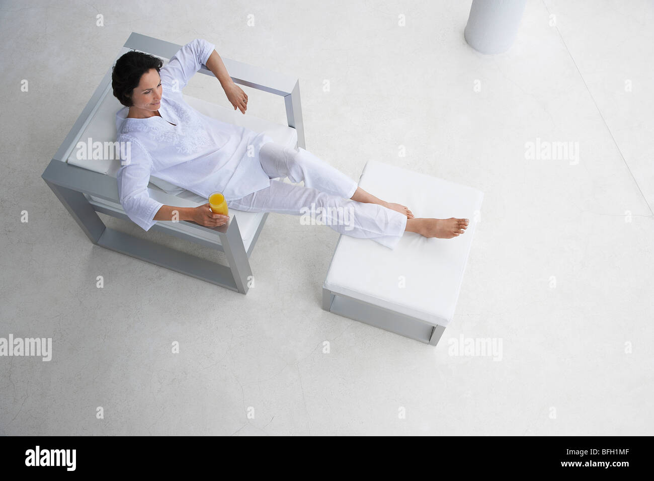 Donna che mantiene un bicchiere di succo di frutta, inclinabile in poltrona, vista in elevazione Foto Stock