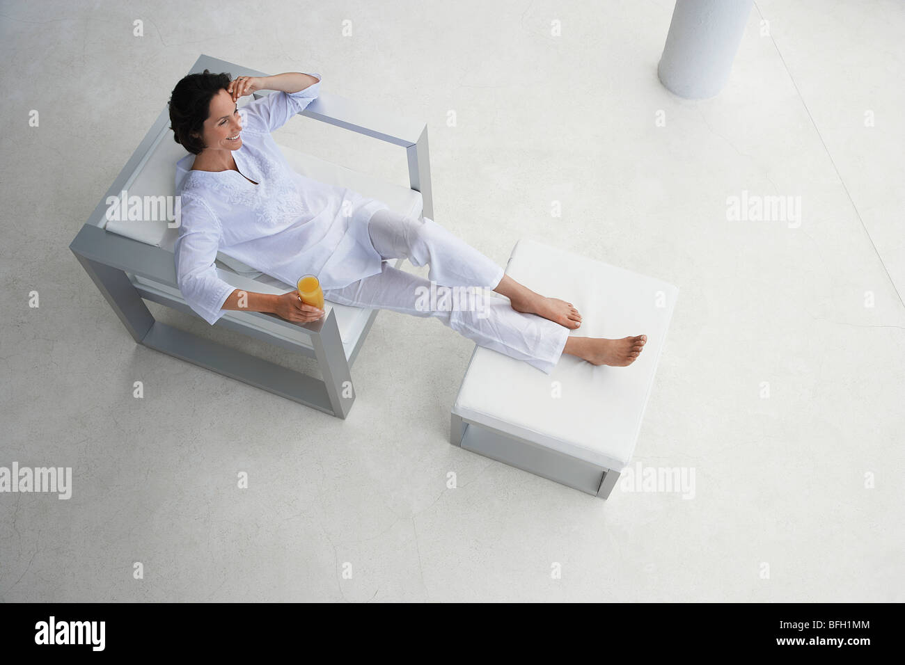 Donna che mantiene un bicchiere di succo di frutta, inclinabile in poltrona, vista in elevazione Foto Stock