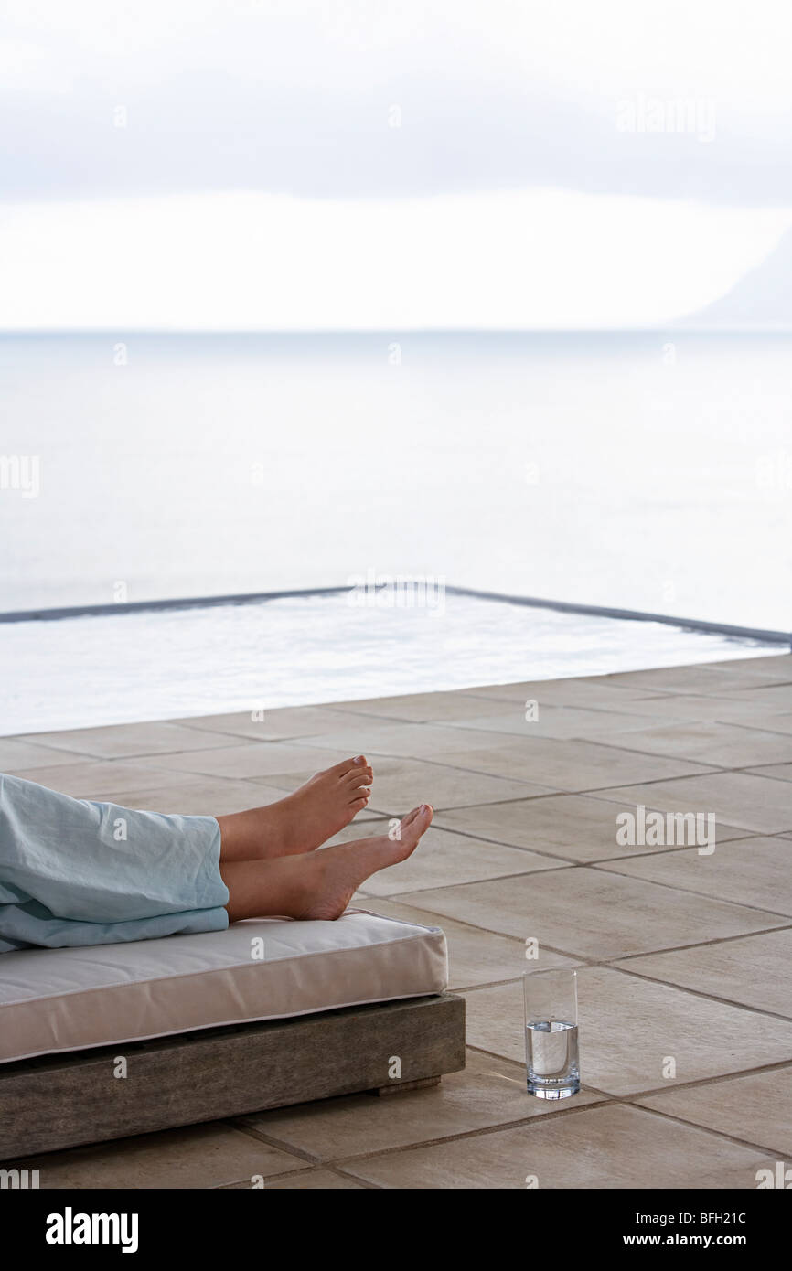 Donna sdraiata sul letto di sun da piscina infinity, sezione bassa Foto Stock
