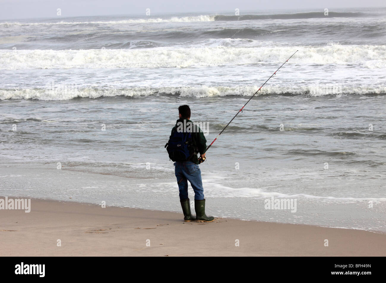 Uomo surf casting su Rainy day su Ocean Beach, Long Island, NY Foto Stock