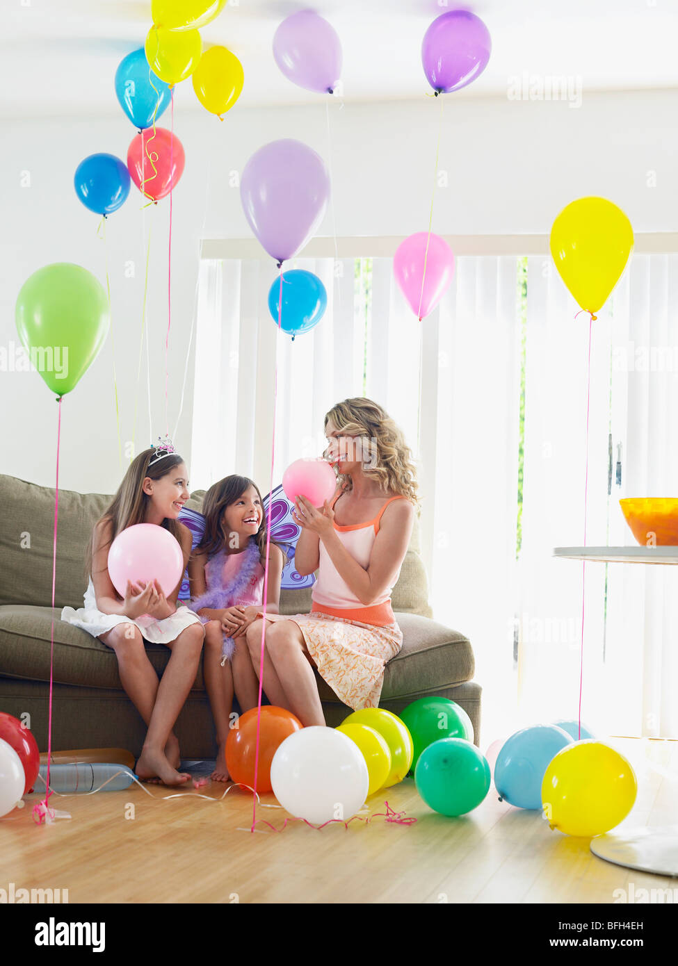 Due ragazze (7-9, 10-12) con la madre seduti sul divano nella stanza piena di palloncini Foto Stock