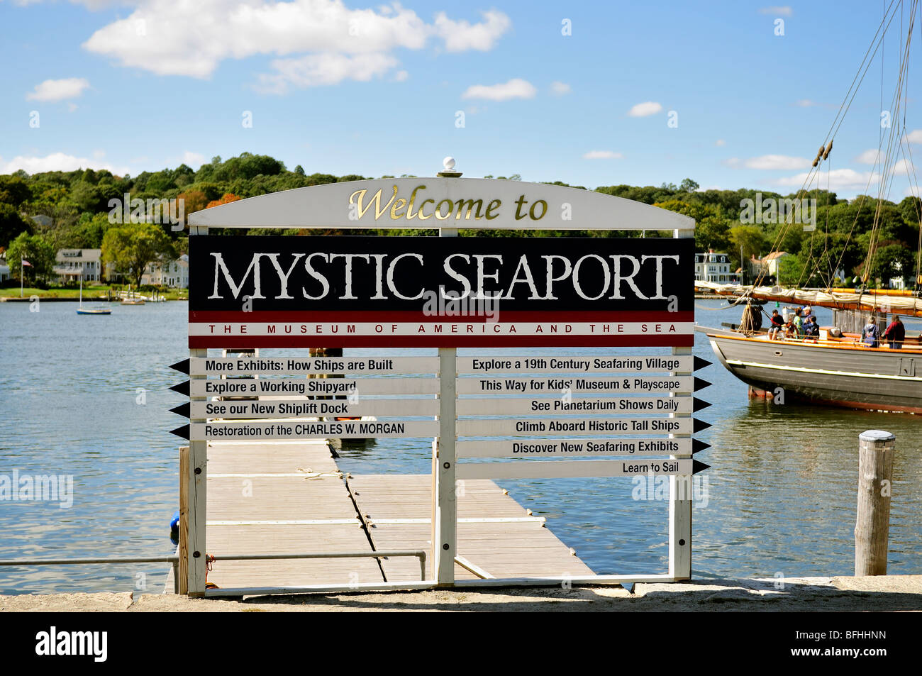 Un segno pubblicità Mystic Seaport, il museo e altre cose da vedere. Dietro il segno è parte di una vecchia nave con i turisti a bordo. Connecticut, Stati Uniti d'America. Foto Stock