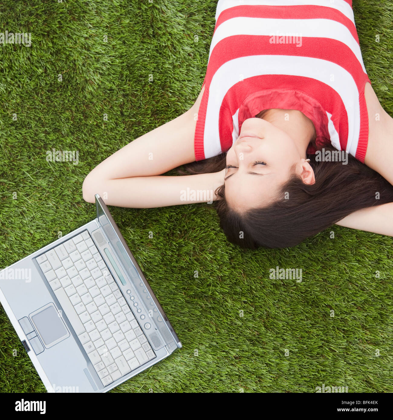 Razza mista donna che dorme in erba con il computer portatile Foto Stock