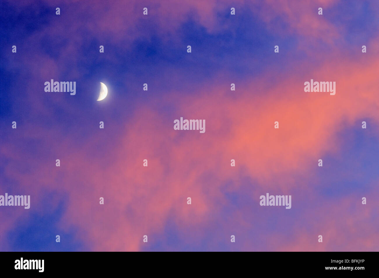 Quarto di luna con Cielo e nubi accese da vivide Tramonto Foto Stock