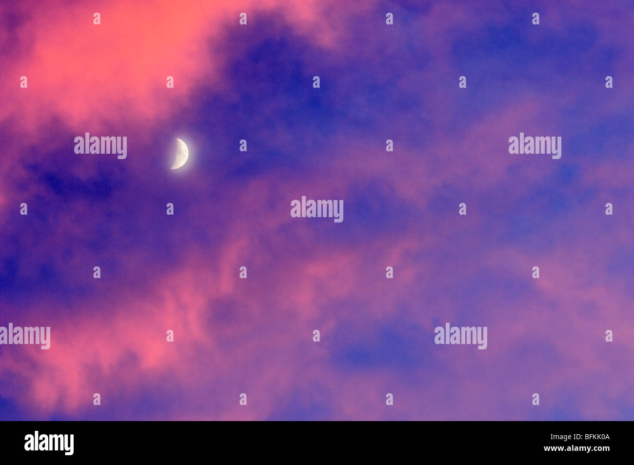 Quarto di luna con Cielo e nubi accese da vivide Tramonto Foto Stock