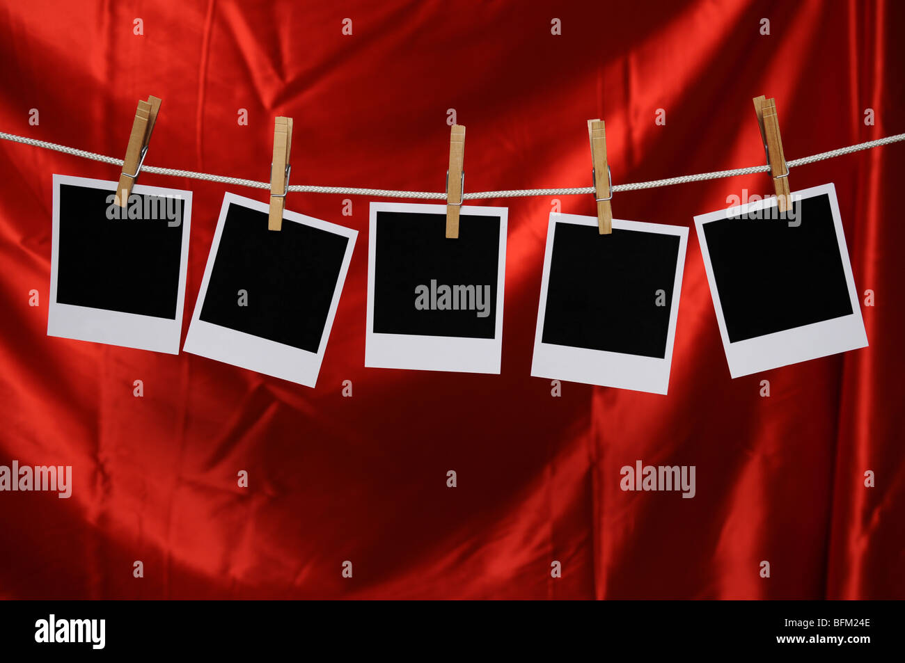 Blank Polaroid foto appese a clothespin oltre un raso rosso sfondo Foto Stock