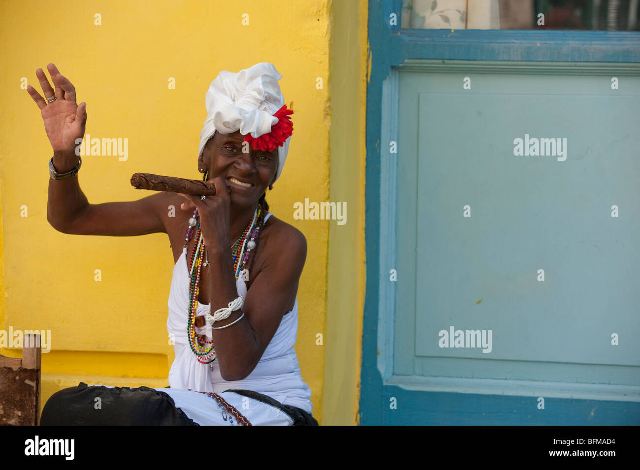 Donna di fumare il sigaro le onde a passerby in Havana Vieja Foto Stock