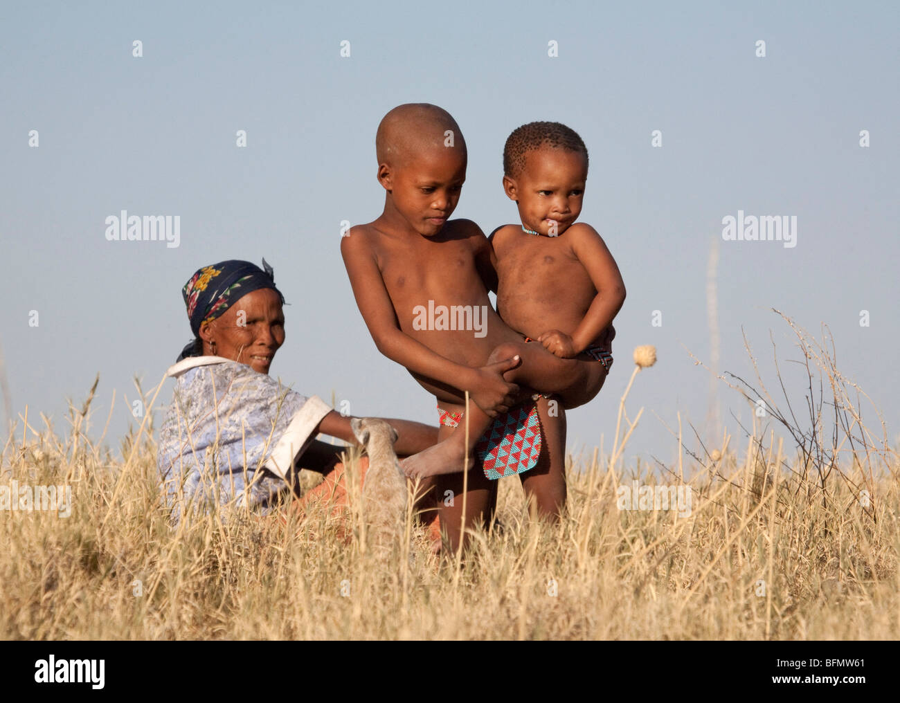 Il Botswana, Makgadikgadi. I Boscimani giocare i bambini in erbe secche del Kalahari, guardati da loro madre. Foto Stock