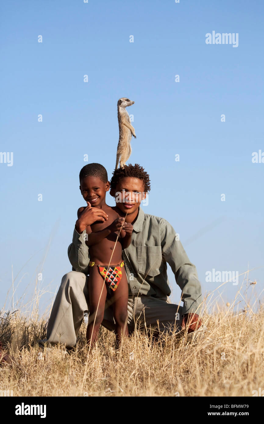 Il Botswana, Makgadikgadi, una guida dei Boscimani con suo figlio. Un meerkat siede sulla sua testa mantenendo la guarda. Foto Stock