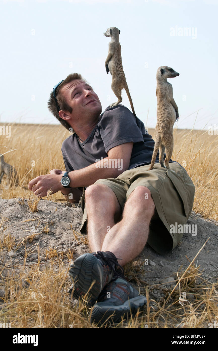 Il Botswana, Makgadikgadi. Un giovane uomo che stabilisce indietro, con meerkats con lui come un punto di osservazione. Foto Stock
