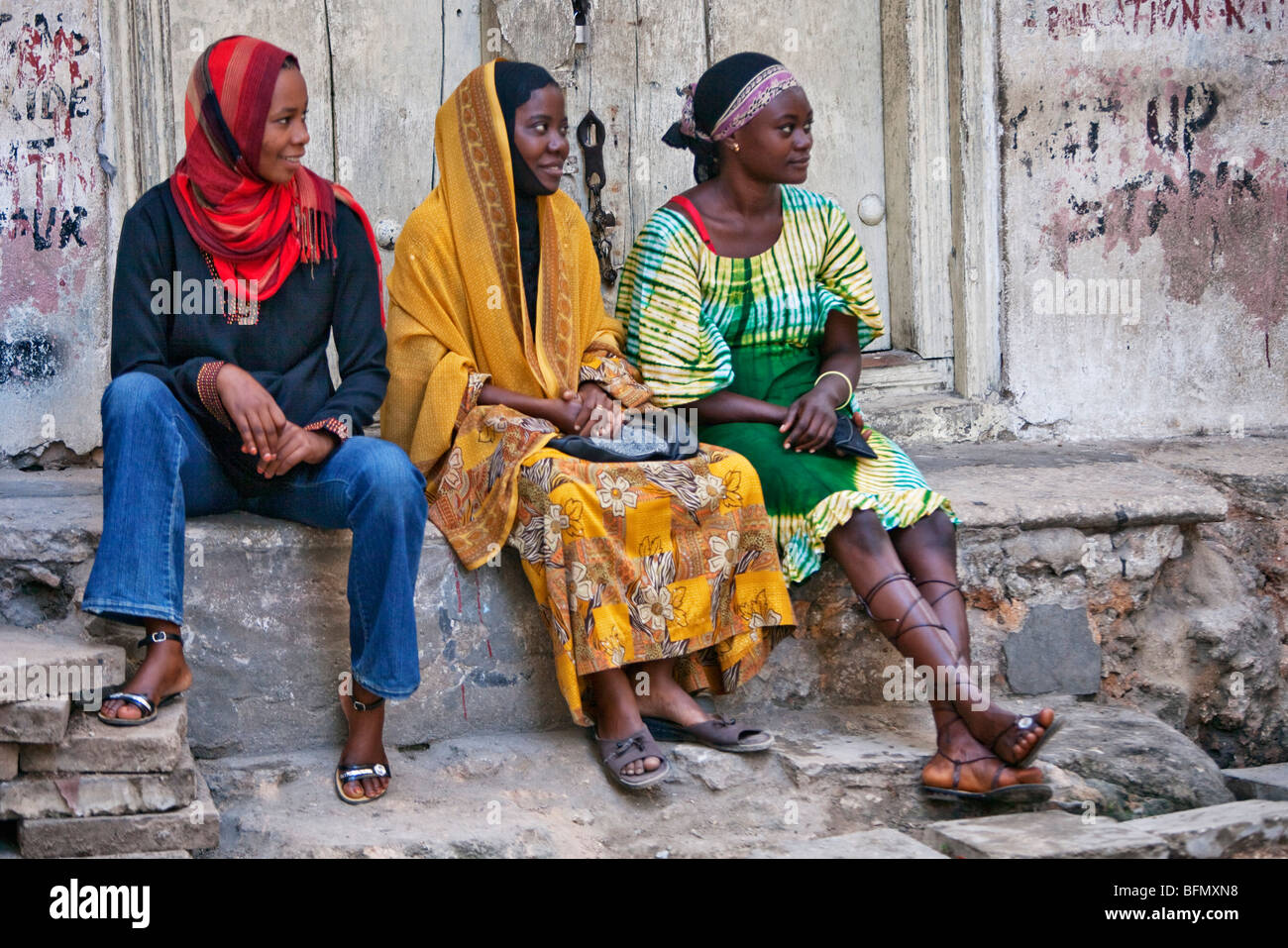 Tanzania, Zanzibar Stone Town. Tre giovani donne rilassarsi su un gradino di pietra nella città di pietra. Foto Stock