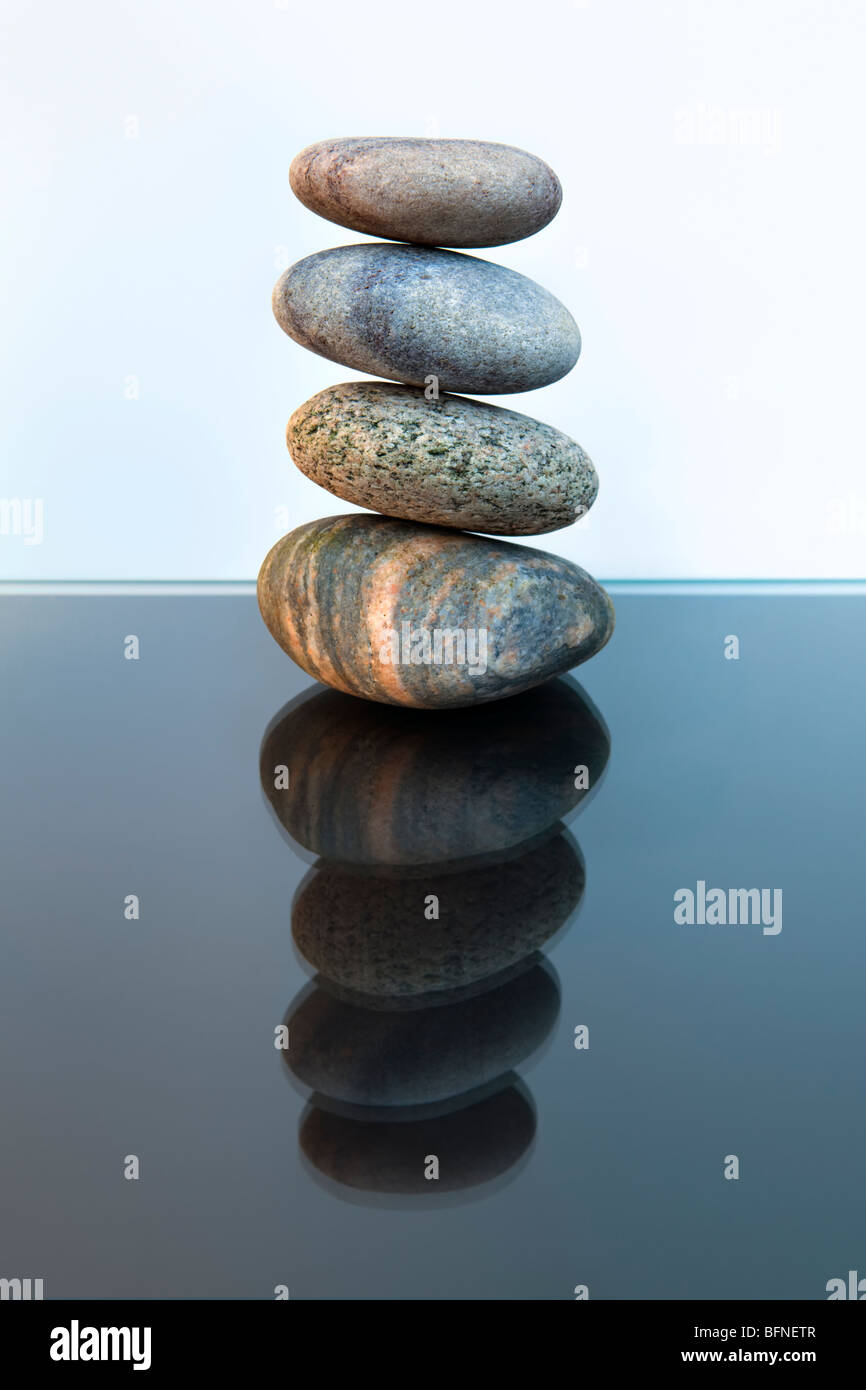 Ancora vita colpo di quattro spiaggia ciottoli equilibrato in una pila di pietra contro nero e sfondo bianco con la riflessione Foto Stock