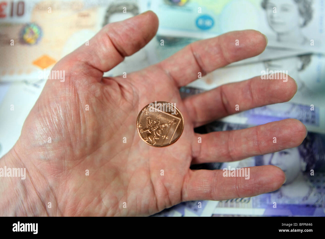 2p di cadere in una mano di una persona anziana, con Sterling note in background Foto Stock