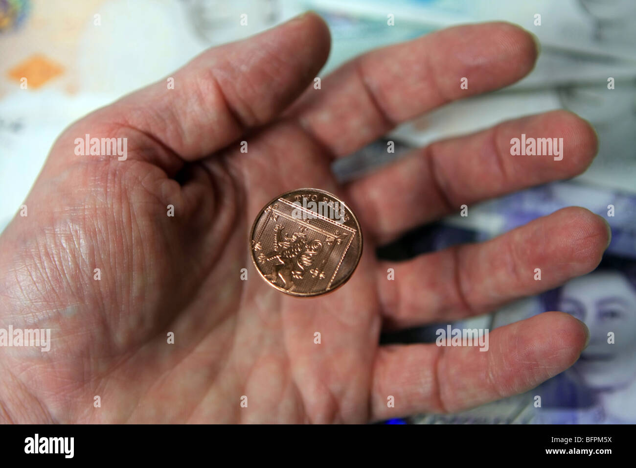 2p di cadere in una mano di una persona anziana, con Sterling note in background Foto Stock