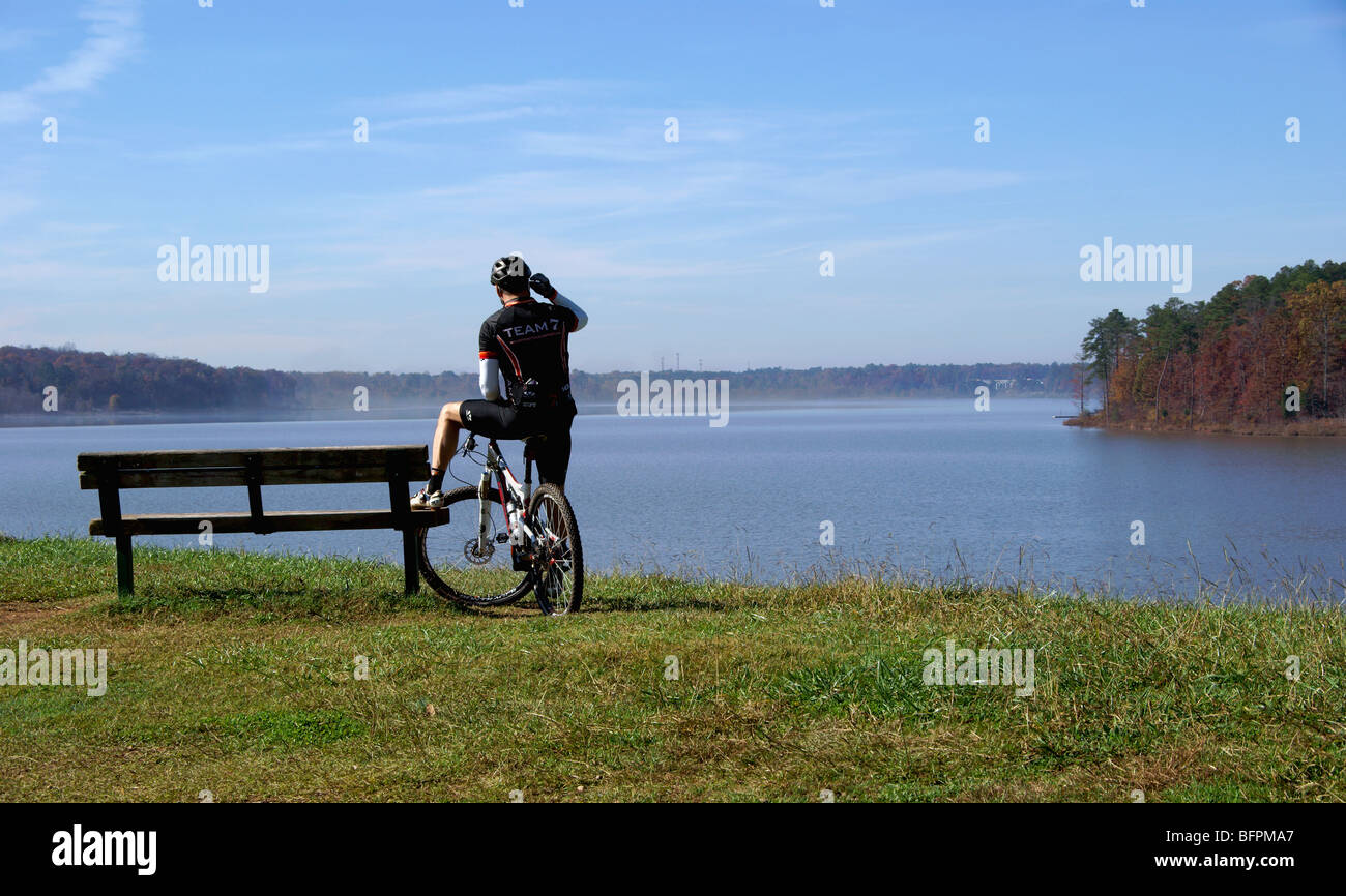Ciclista (Silhouette) guardando la nebbia sollevare da un lago tenendo su un telefono cellulare Foto Stock