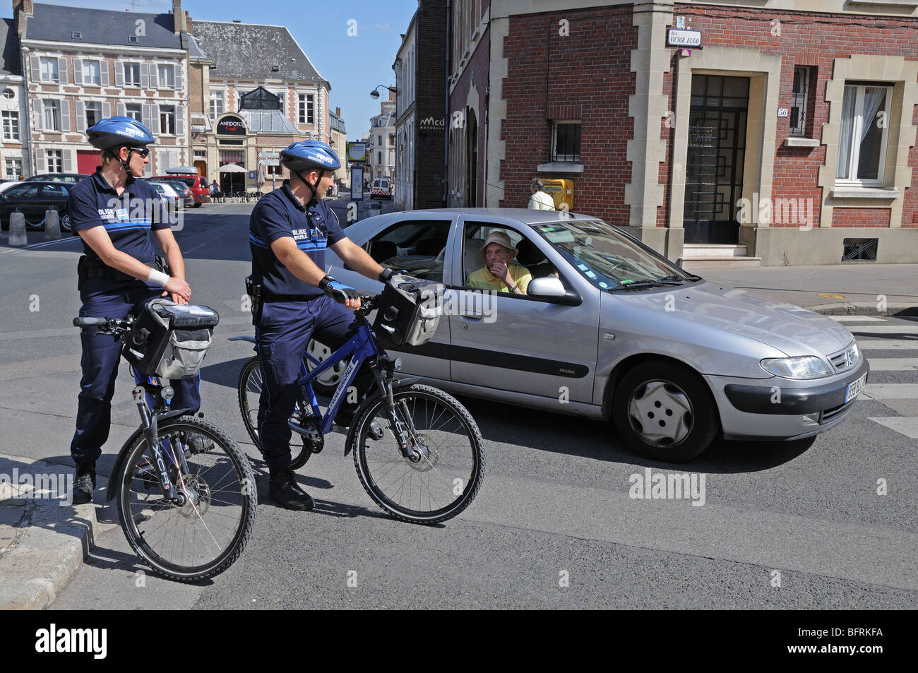 Due forze di polizia municipale municipale sulle biciclette sosta per aiutare un automobilista passa in argento Citroen auto trovare la sua strada in Amiens Francia Foto Stock