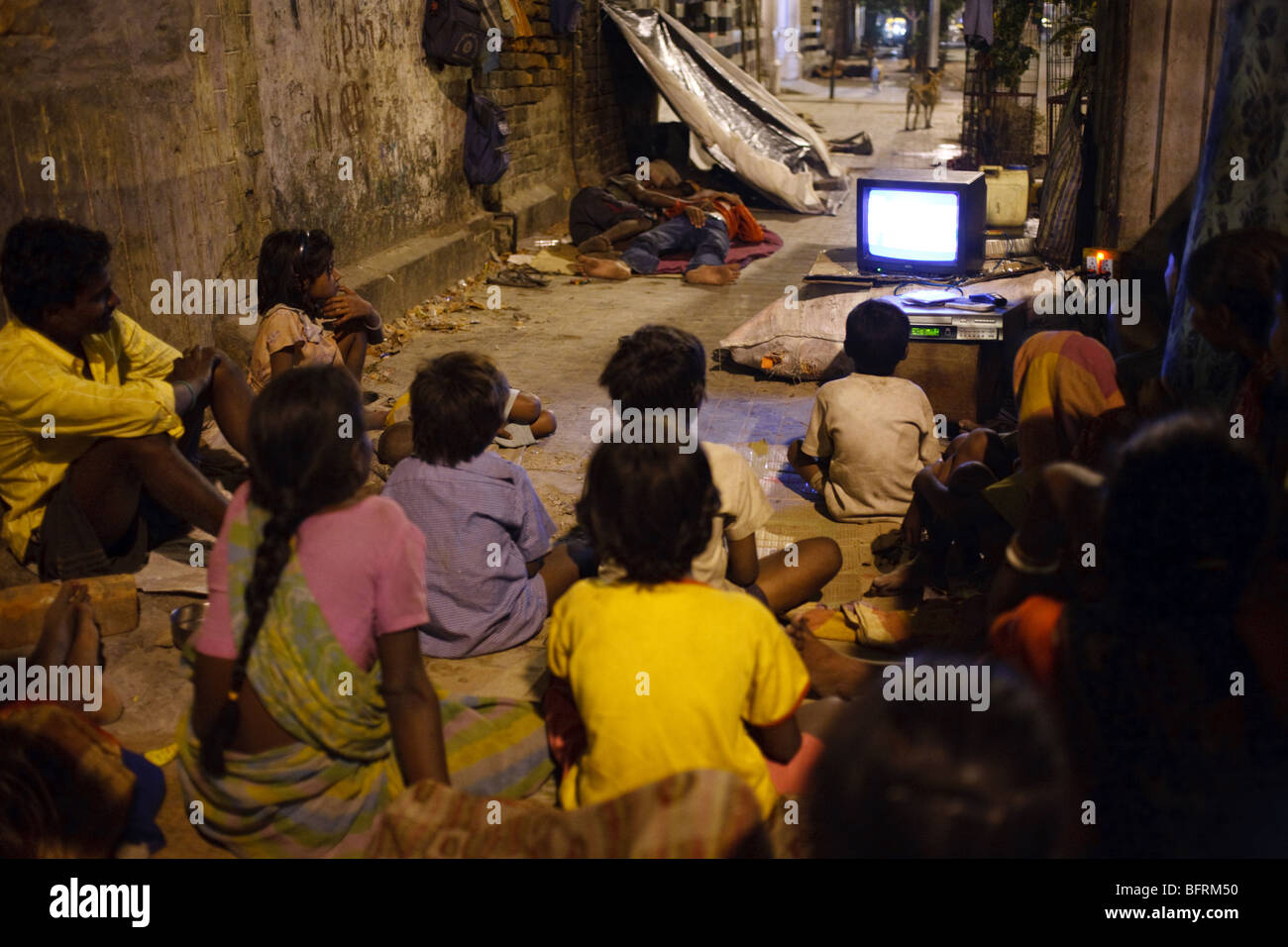 Persone senza dimora guarda la TV di notte su un marciapiede in Kolkata, India Foto Stock