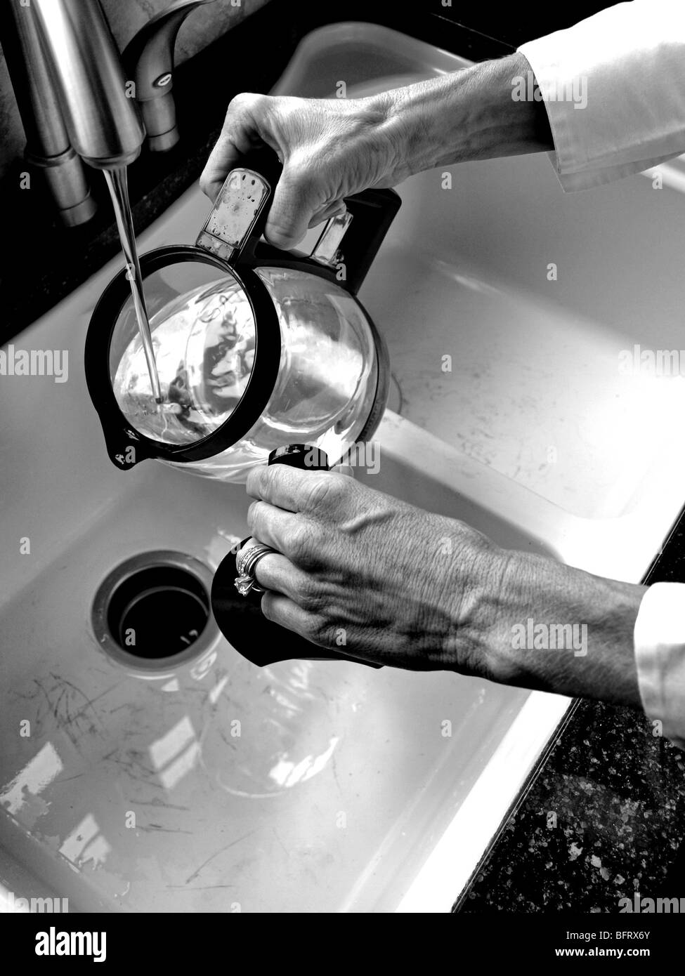 Donna mettendo acqua in caraffa di caffè brocca dal rubinetto nel lavello in cucina close-up Foto Stock