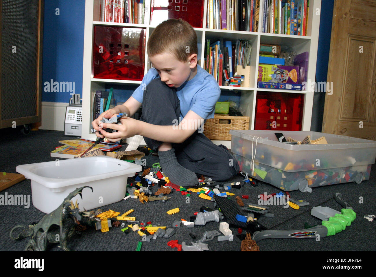 Ragazzo giovane riordino via i giocattoli nella sua camera da letto Foto Stock
