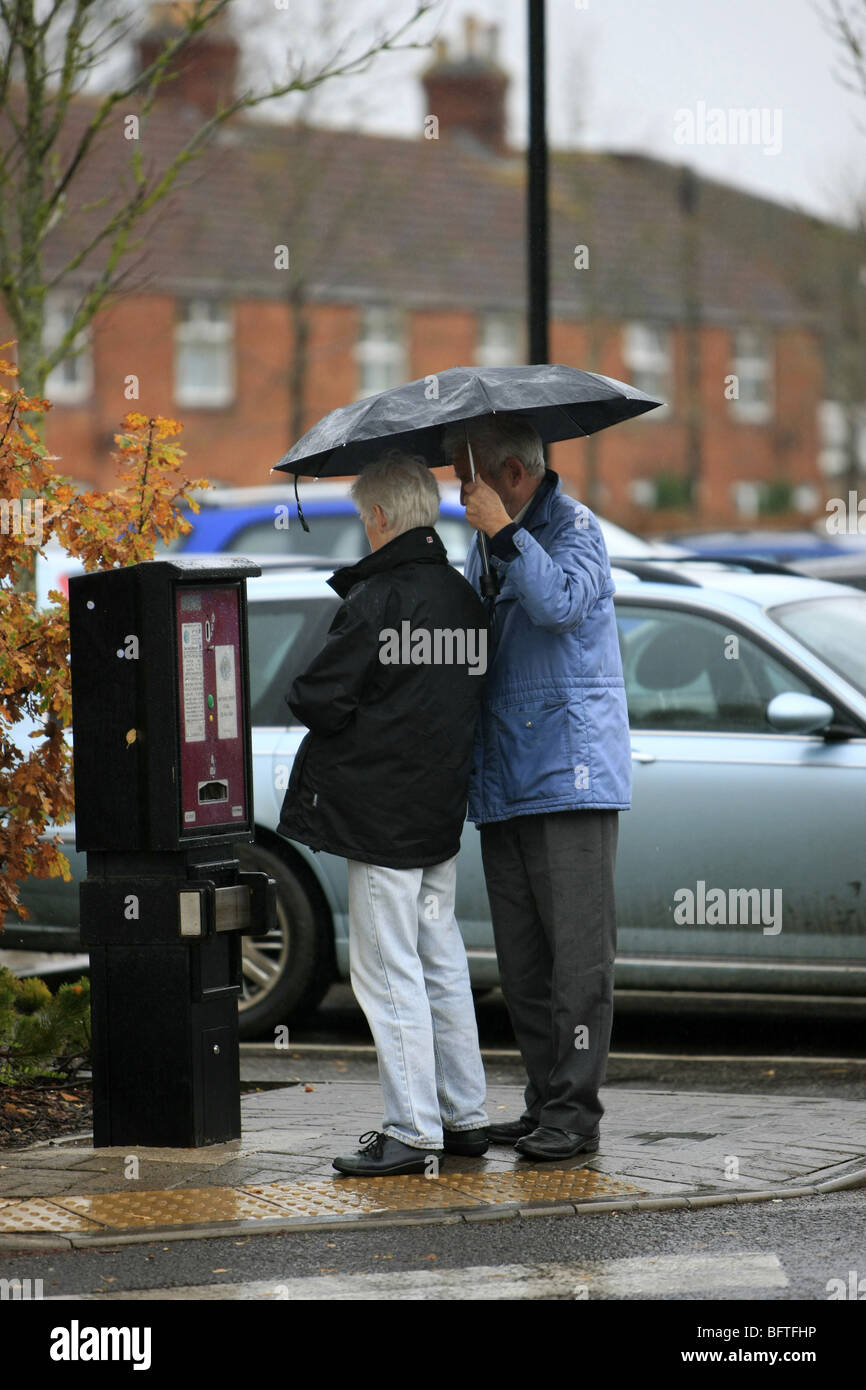 L uomo e la donna il ricovero sotto un ombrello pur pagando per un parcheggio ticket Foto Stock