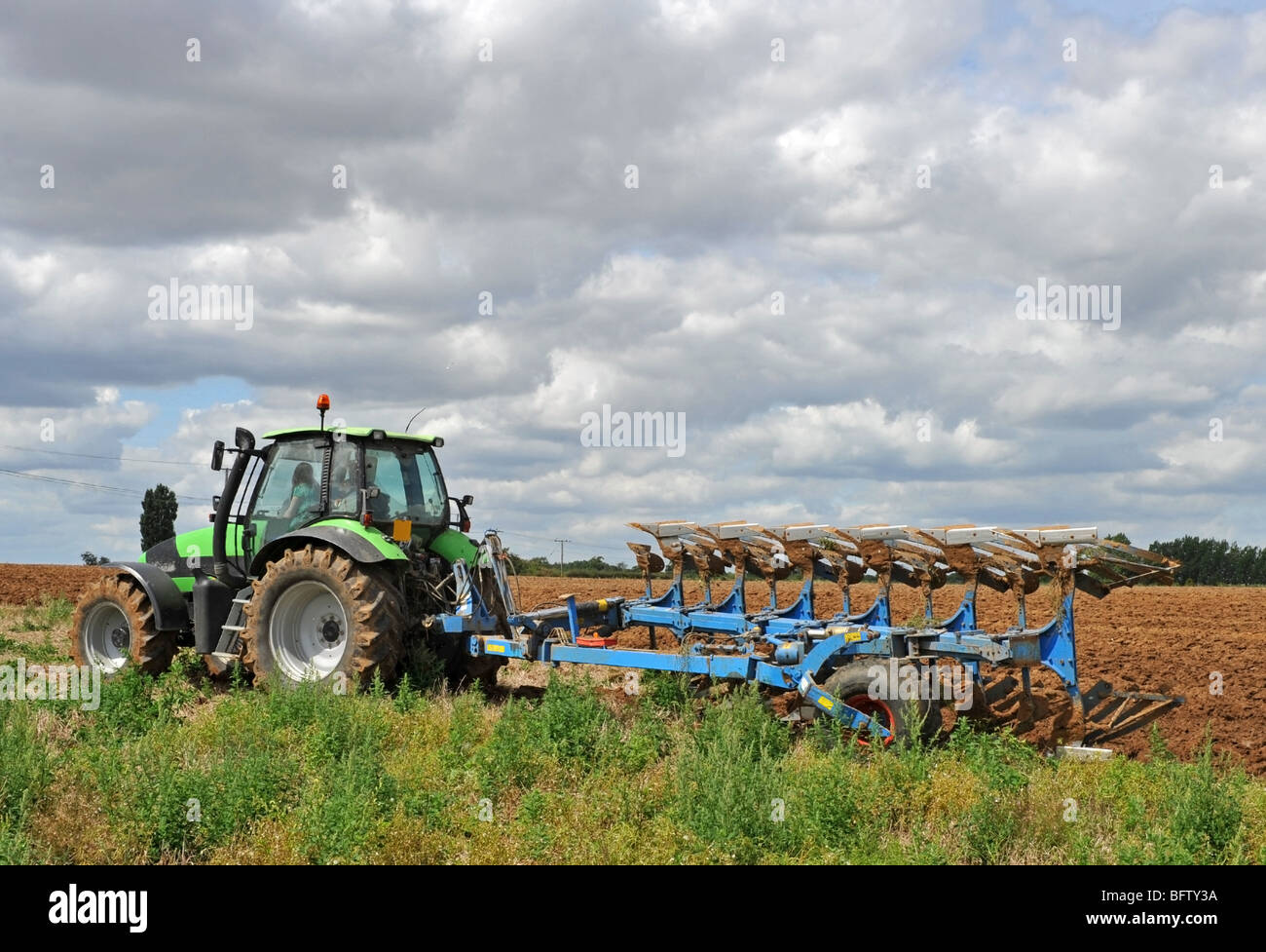 Trattore verde arando un campo pronto per la semina. Foto Stock