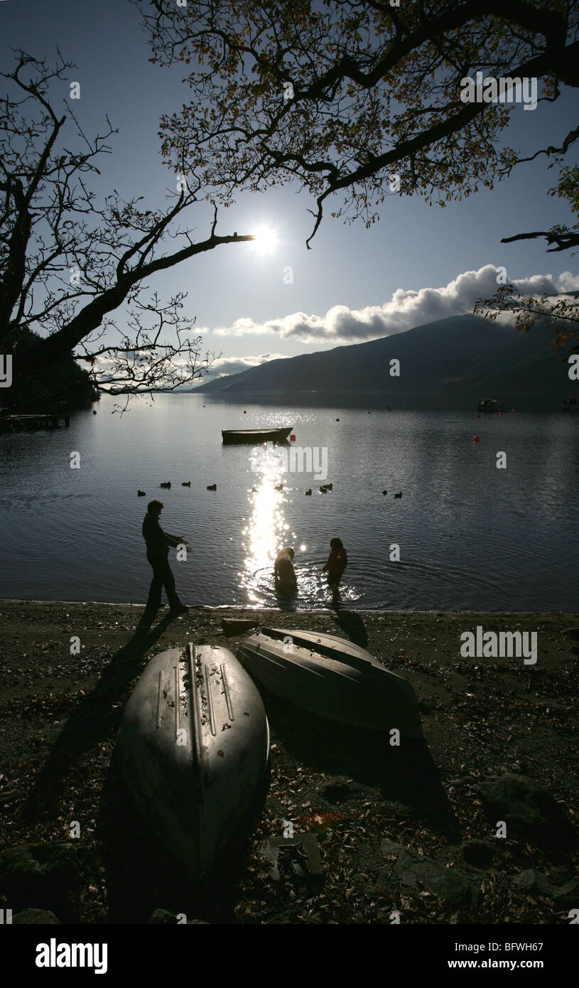 Area di Loch Lomond, Scozia. Vista profilarsi di una figlia della madre e cane sguazzare nell'acqua a Rowardennan rive. Foto Stock