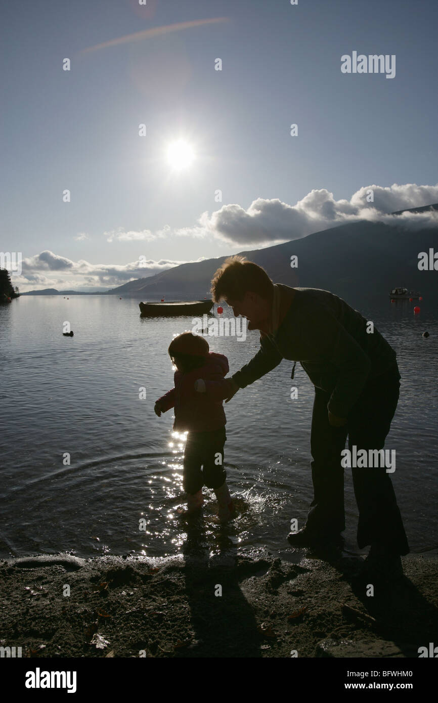 Area di Loch Lomond, Scozia. Vista profilarsi di una madre e figlia sguazzare nell'acqua a Rowardennan rive Foto Stock