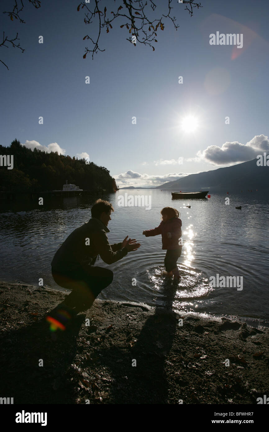 Area di Loch Lomond, Scozia. Vista profilarsi di una madre e figlia sguazzare nell'acqua a Rowardennan rive. Foto Stock