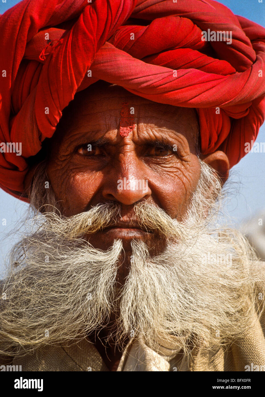 Un anziano barbuto Rajasthani uomo con un turbante rosso durante il Pushkar fiera del bestiame nei deserti del Rajasthan in India Foto Stock