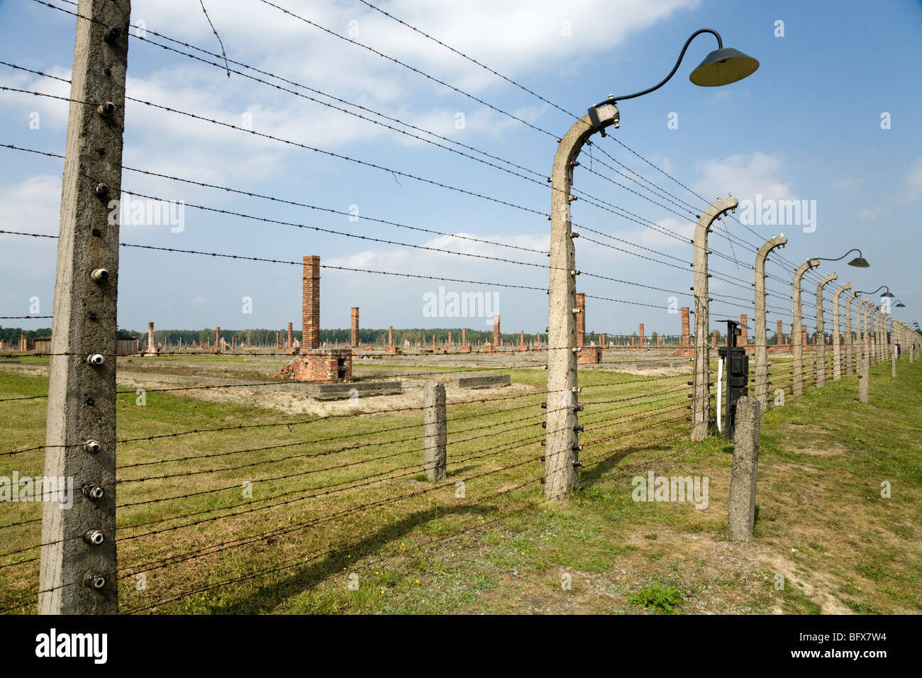 Recinzioni perimetrali / Birkenau (Auschwitz II Birkenau) nazista di morte nel campo di Oswiecim, Polonia, & ciminiere in laterizio da case a castello dietro Foto Stock