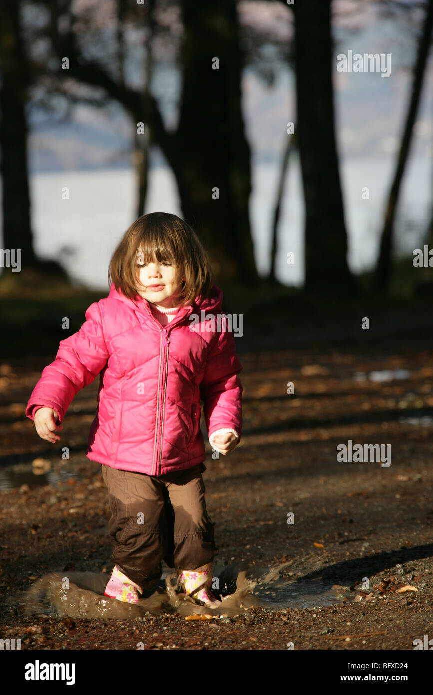 Ragazza giovane di saltare in una pozzanghera con il Loch Lomond in background. Foto Stock