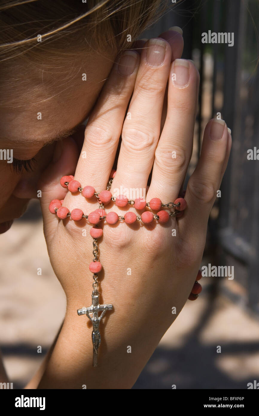 Giovane donna orante con il rosario nelle sue mani. Foto Stock