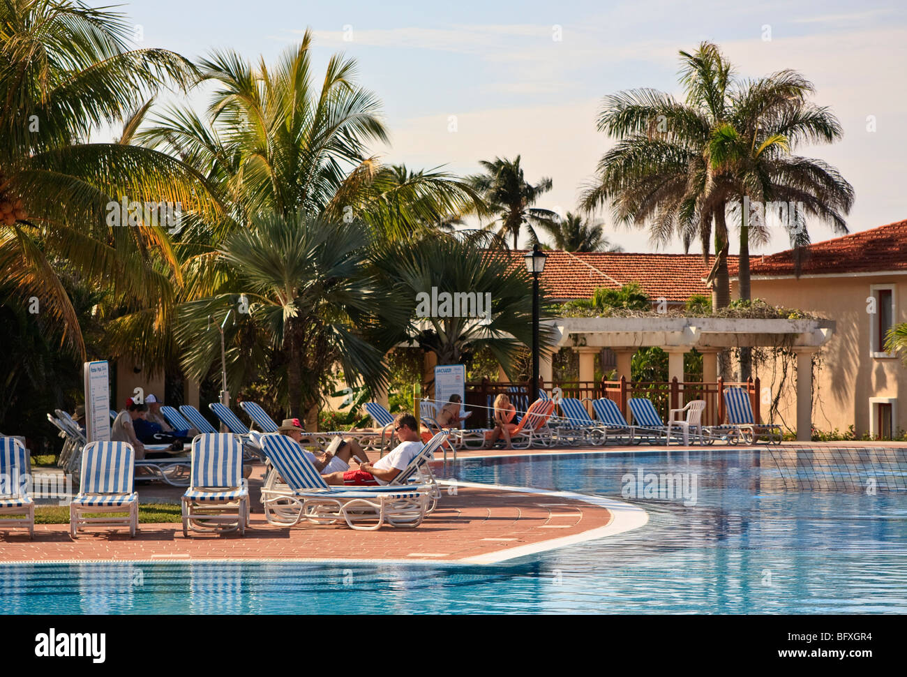 La gente che legge i libri per la piscina di un resort caraibico, Cuba Foto Stock