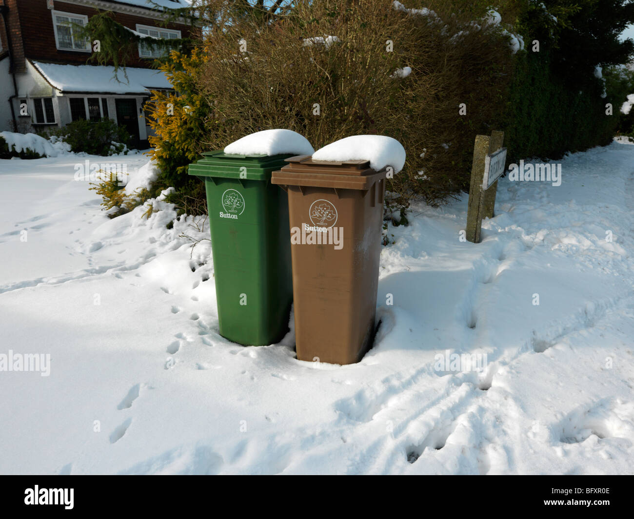 Verde e Marrone scomparti Wheelie in neve fuori casa in attesa di raccolta Cheam Surrey in Inghilterra Foto Stock
