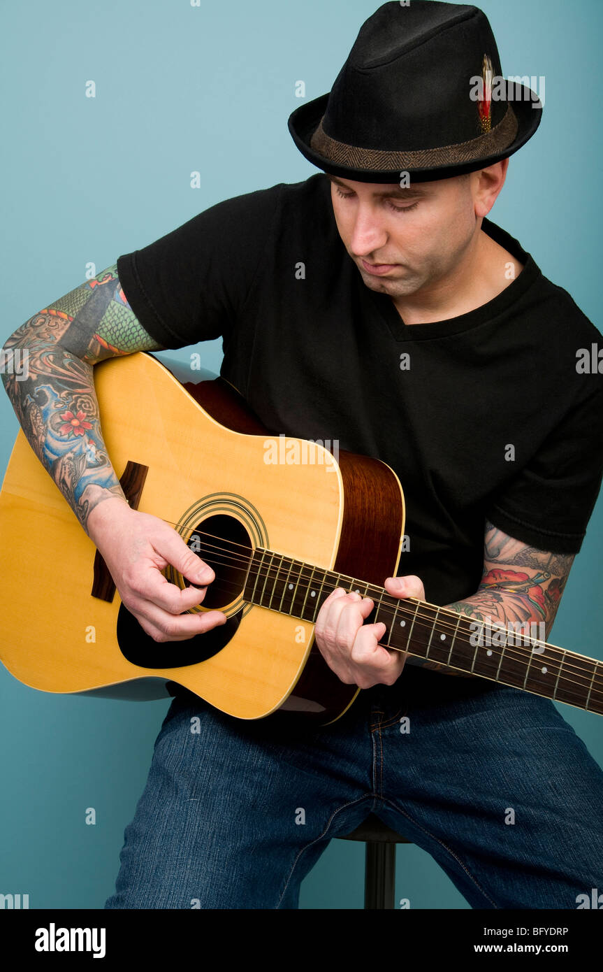 Uomo con tatuaggi a suonare la chitarra Foto Stock