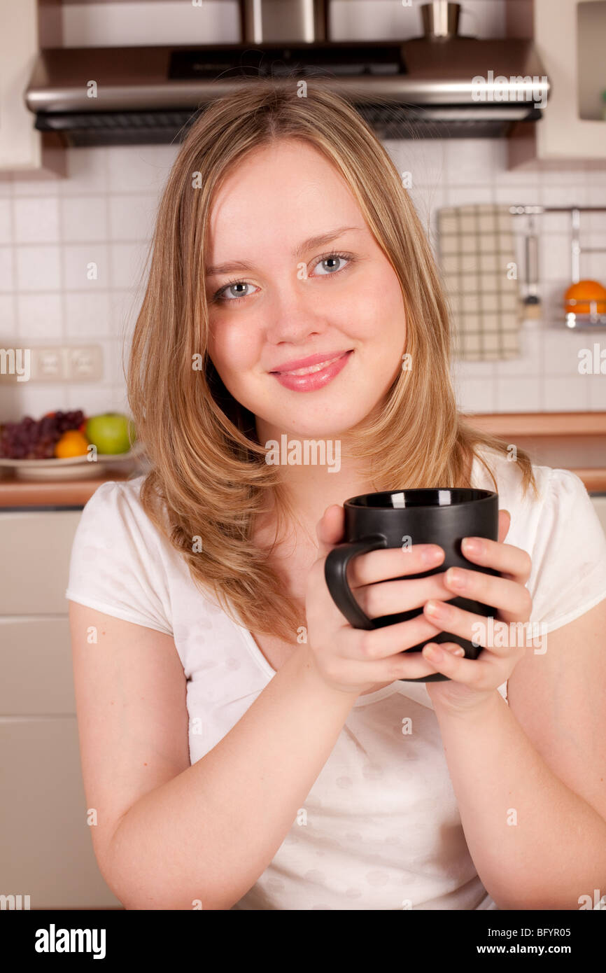 Giovane donna felice bere caffè o tè in cucina Foto Stock