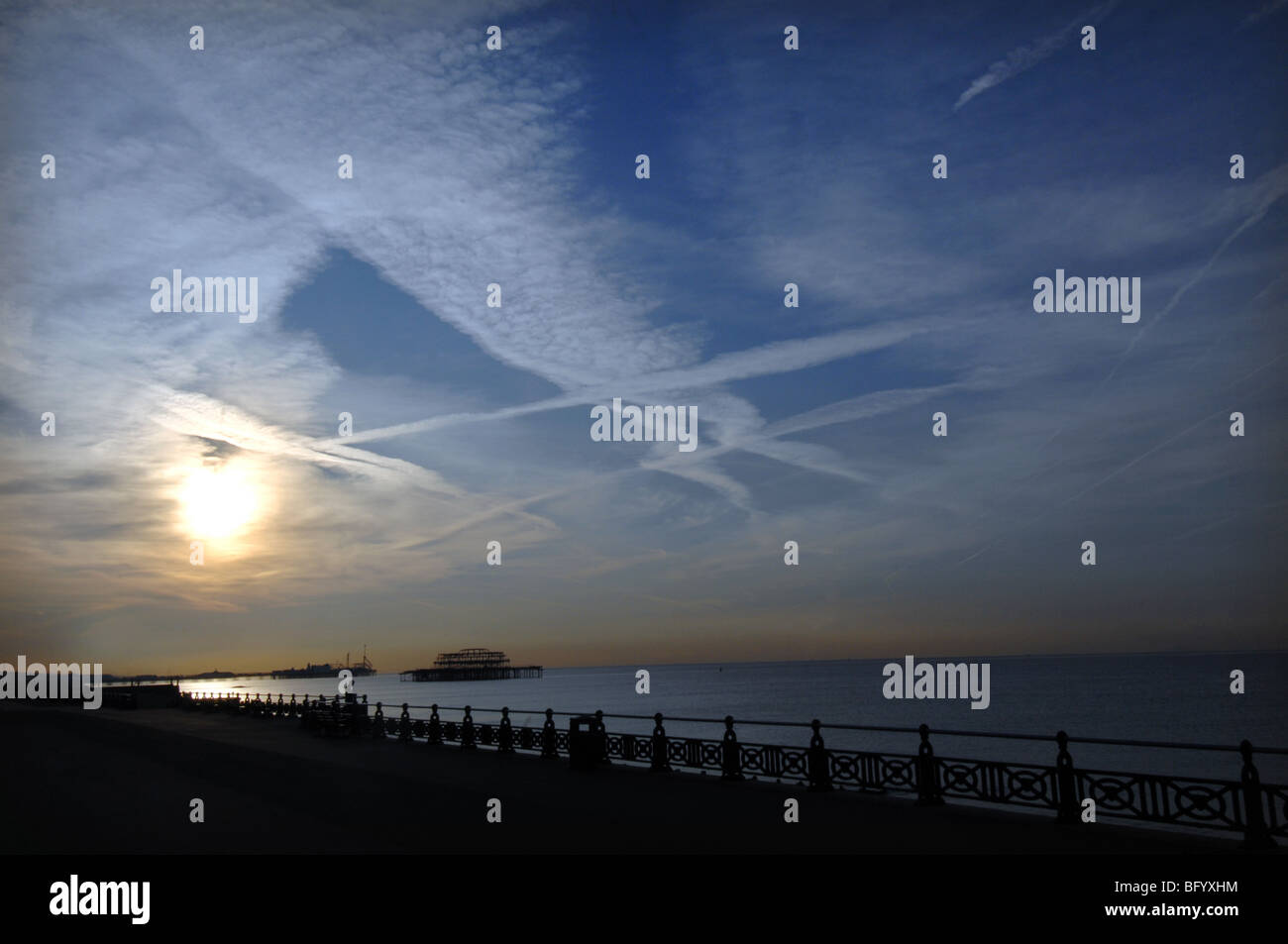 Alba sul lungomare di Brighton con jet striature nel cielo e il molo di ponente profilarsi in lontananza. Foto Stock