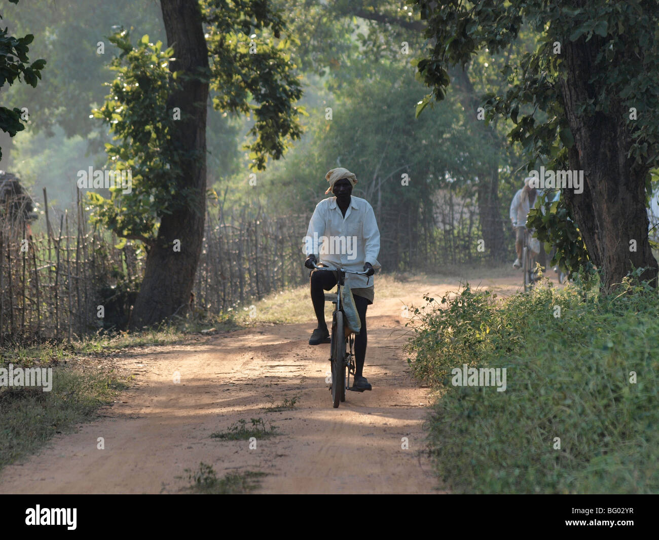 Indian abitante in costume locale escursioni in bicicletta lungo la pista polverosa in patch di pezzata sunshine con fogliame retroilluminato in illuminazione soffusa Foto Stock