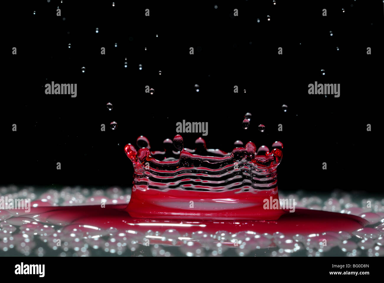 Una goccia di rosso acqua formando un coronet come esso cade in uno strato superficiale di liquido Foto Stock