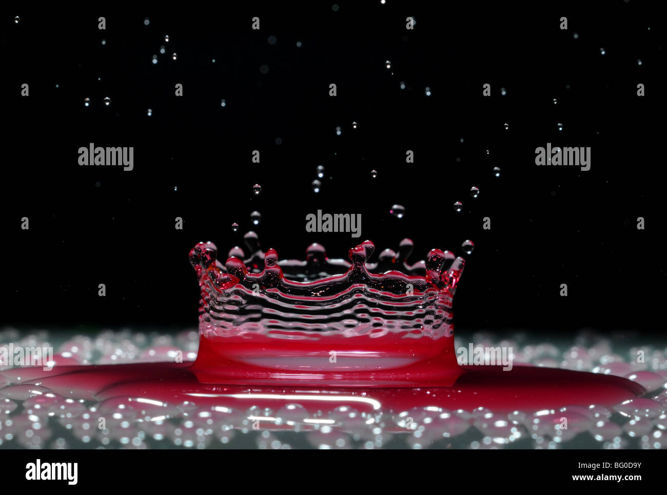 Una goccia di rosso acqua formando un coronet come esso cade in uno strato superficiale di liquido Foto Stock