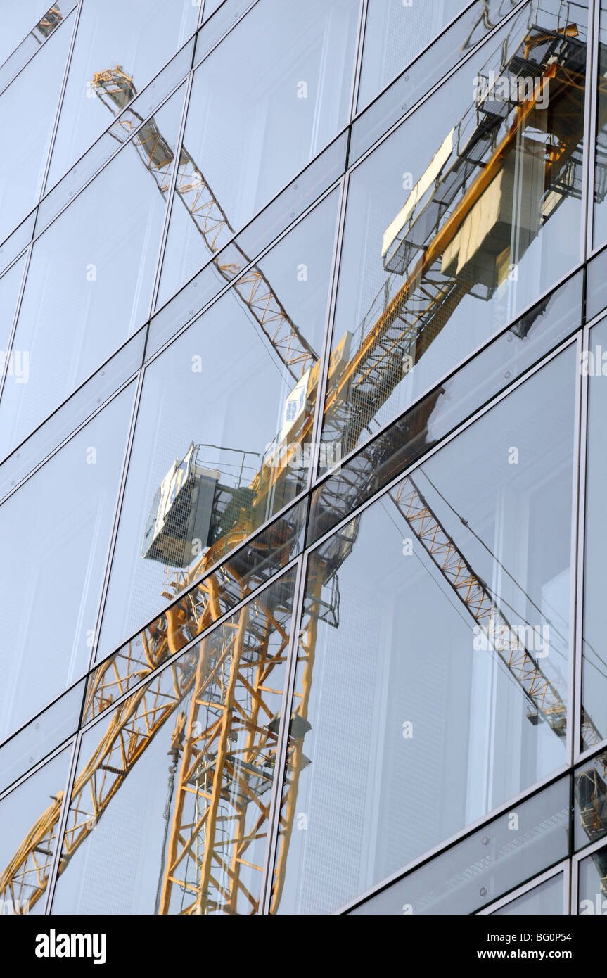 La riflessione di gru da cantiere nella finestra del grattacielo di vetro. Berlino. Foto Stock