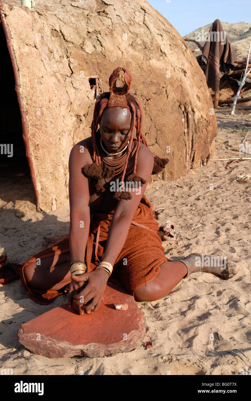 Donna della tribù Himba macinazione di pigmento per la decorazione del corpo, Kaokoland, Namibia, Africa Foto Stock