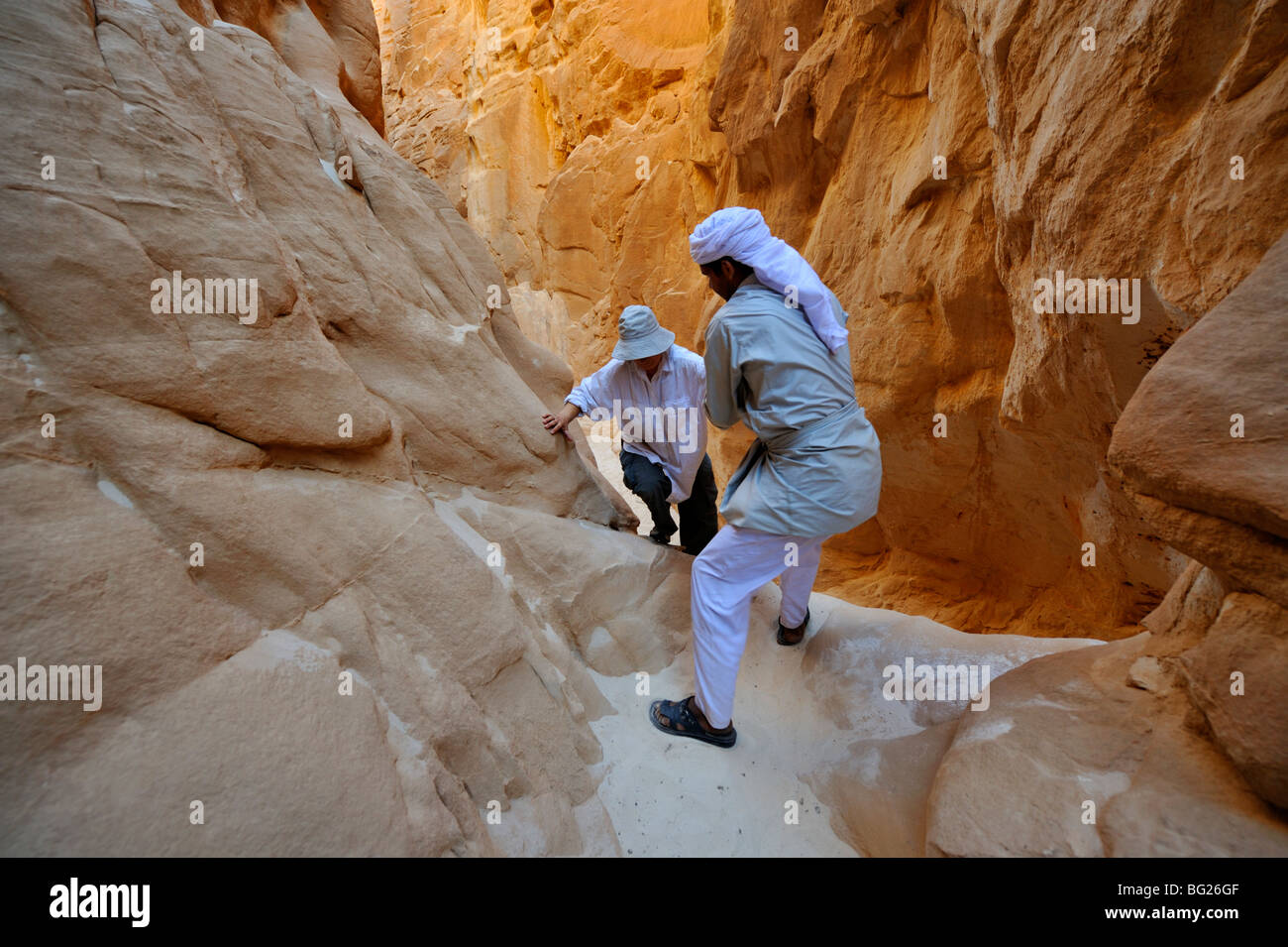 Guida beduina aiutando turista in molto strette Abu Hamata Canyon, Sud nel deserto del Sinai, Egitto Foto Stock