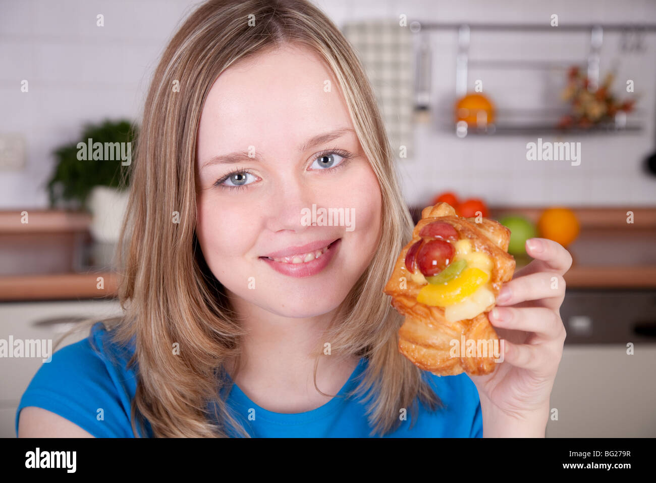 Bella donna sorridente trattiene il dolce bun decorate con frutti in cucina interna. Foto Stock